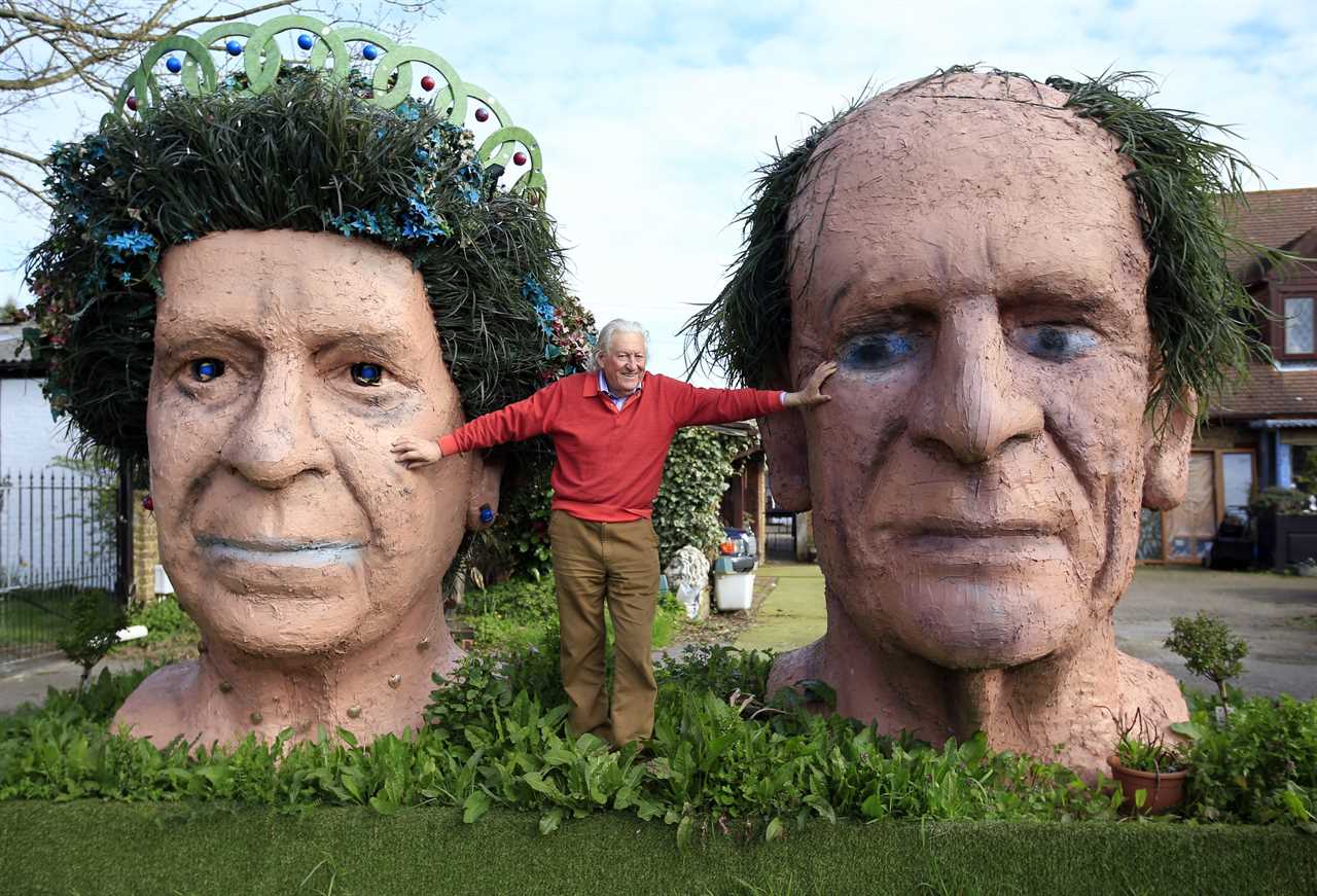 Ben Bennett stands between terracotta head sculptures of Queen Elizabeth and the Duke of Edinburgh