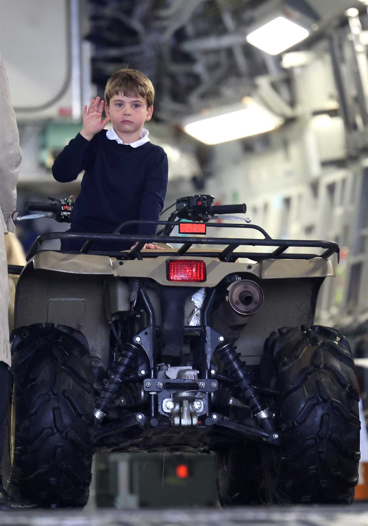 Prince Louis gives a shy wave as Kate helps him climb onto a quad bike during family day out with siblings at air show