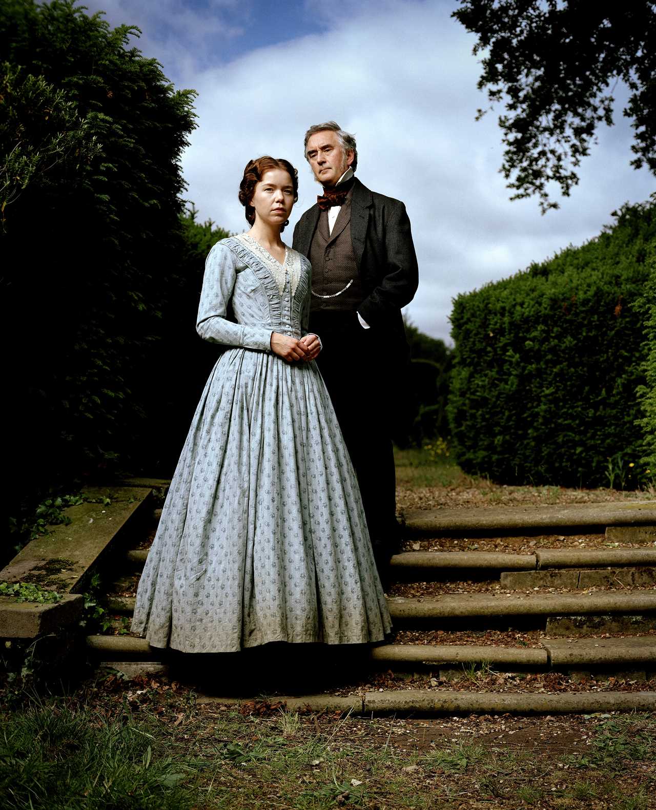 a woman in a blue dress stands next to a man in a black suit