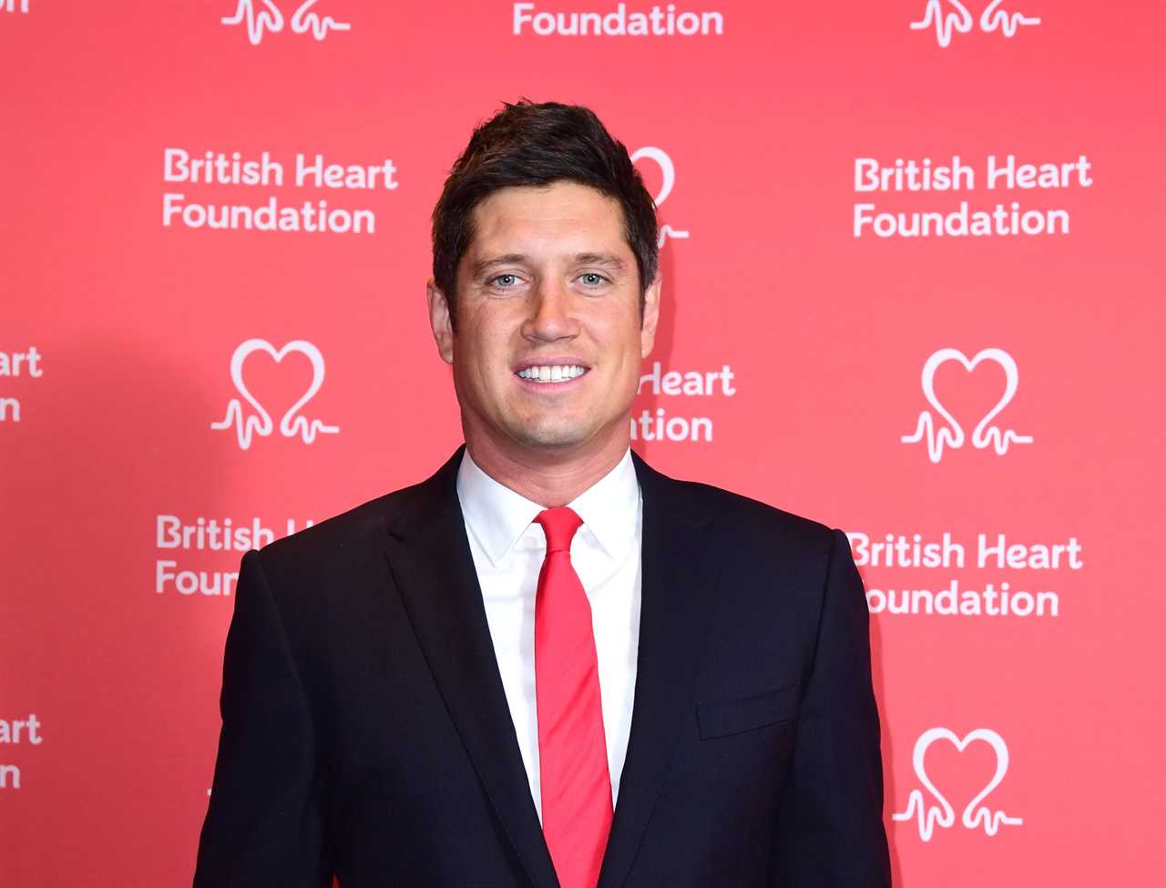 a man in a suit and tie stands in front of a british heart foundation wall